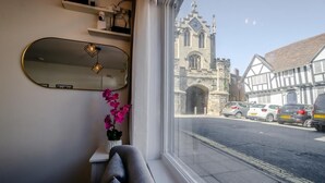 A room with a large window, a mirror, a potted orchid, and a view of a historic building. - 2 Bed in Warwick (oc-c41051) (Warwick)