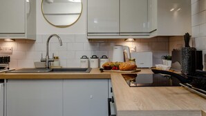 A modern kitchen with white cabinets, a round mirror, a Bosch coffee machine, and a wooden countertop. - 2 Bed in Warwick (oc-c41051) (Warwick)