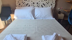 Ein ordentlich bezogenes Bett mit weißen Leinen, ein dekoratives Kopfteil und zwei Handtücher auf dem Bett.