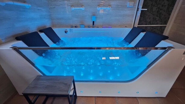 Ein Whirlpool mit vier schwarzen, gepolsterten Sitzen, einem kleinen Holzschemel und einer Steuerung.