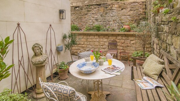 Un patio con un tavolo rotondo, sedie, una panchina e una statua.
