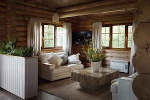 A log cabin interior with a sofa, a coffee table, a TV, and a potted plant.