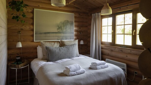 Een gezellig houten slaapkamer met een bed, twee bedlampen, een radiator en een raam met gordijnen.