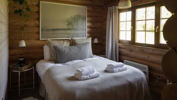 Une chambre confortable, aménagée dans un chalet en bois, avec un lit, deux lampes de chevet, un radiateur et une fenêtre avec des rideaux.