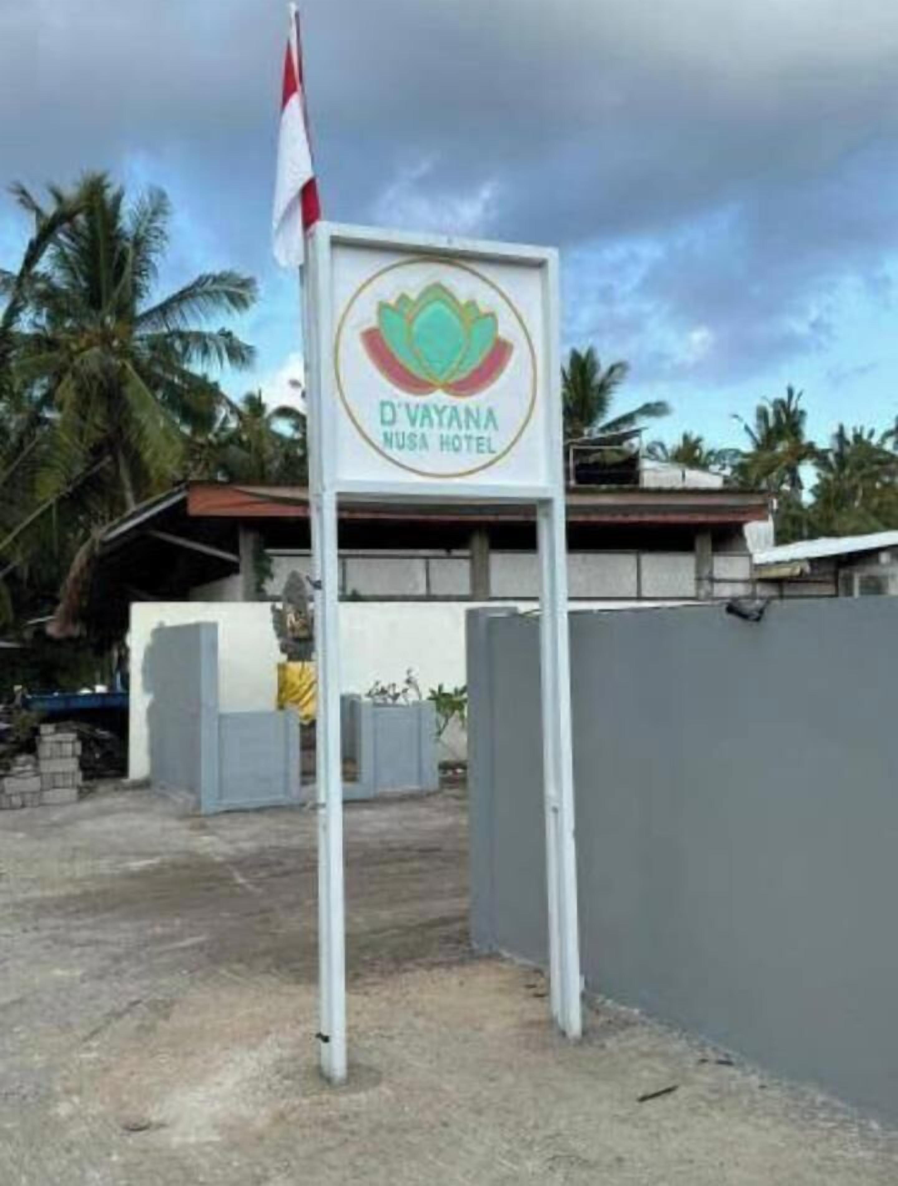 A sign for D'Vayana Nusa Hotel with a logo, a flag, and a gated entrance.