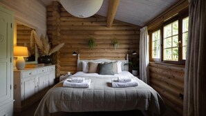 A log cabin bedroom with a bed, bedside lamps, a dresser, and a window with curtains.