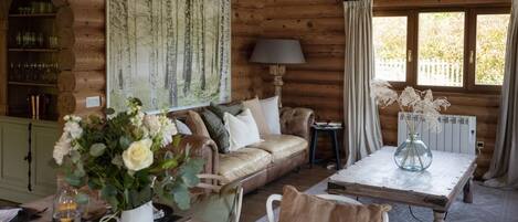 Interior acogedor de una cabaña de madera con comedor, sofá, un cuadro y una mesa dispuesta para el desayuno.