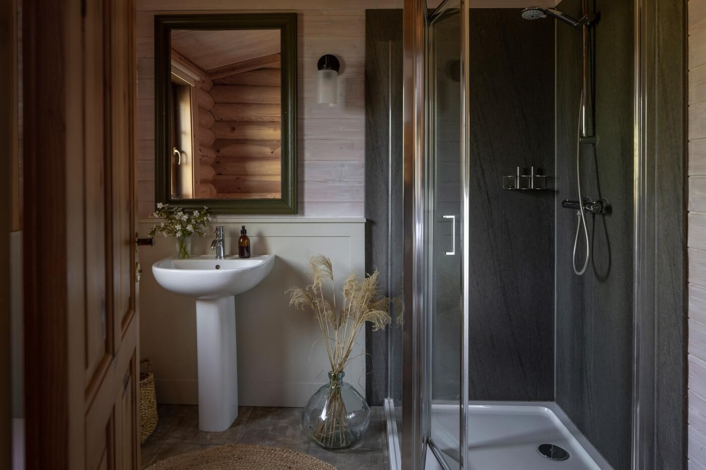 Une salle de bain avec une douche à parois de verre, un lavabo blanc et un miroir avec un cadre vert.