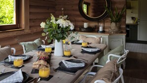 A wooden cabin interior with a dining table set for breakfast, including plates, glasses, and a vase of flowers.