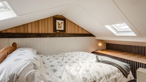 Ein Schlafzimmer mit schrägen Wänden, einem Bett mit gemustertem Überwurf, einem Nachttisch mit Lampe und einem gerahmten Bild an der Wand.