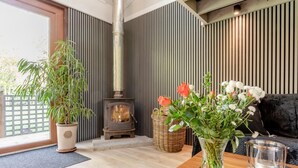 Ein gemütliches Wohnzimmer mit Kaminofen, einer Couch, einem Tisch mit Blumenvase und einer Topfpflanze.