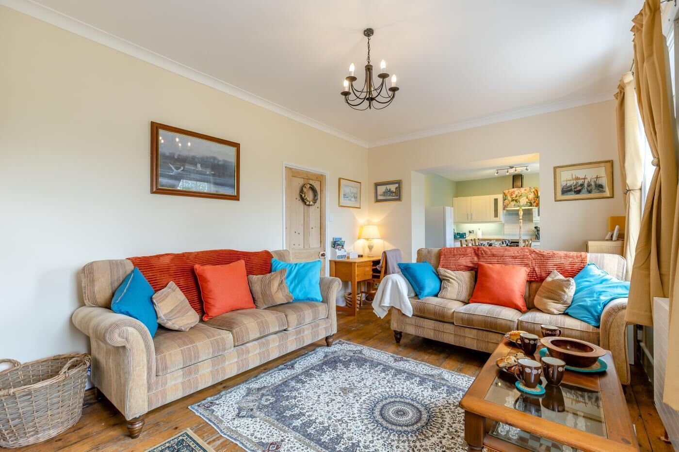 A living room with two sofas, a chandelier, a rug, and a kitchen in the background.