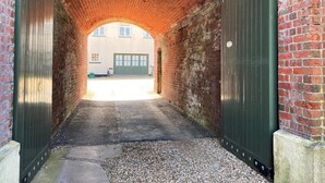 A brick tunnel with two green doors, a gravel path, and a building with windows in the background. - 3 Bed in Freshwater (oc-78099) (Freshwater)