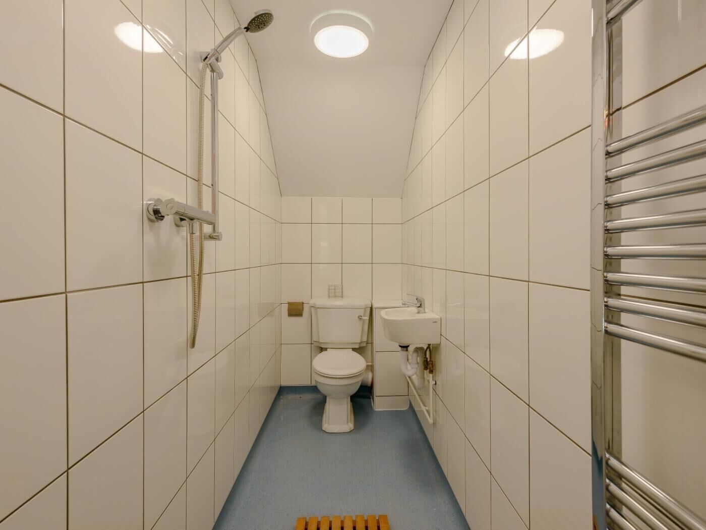 Ett litet, modernt badrum med vita kakelplattor, en toalett, ett handfat och en dusch.