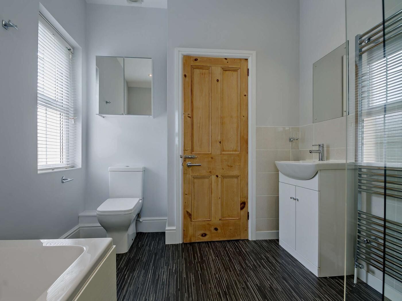 Een badkamer met een houten deur, witte sanitair en een badkuip, plus een douchecabine met glazen wanden.