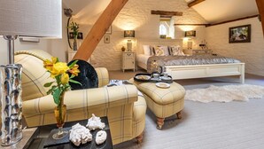 Quarto de sótão com cama, sofá, mesa e objetos decorativos, e uma luminária.