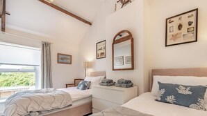 Un dormitorio con dos camas, ventana con vistas, techo con vigas de madera y cuadros en las paredes.