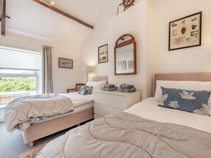 A bedroom with two beds, a window with a view, a wooden beam ceiling, and framed pictures on the walls. - 3 Bed in Tenby (oc-fb189) (Tenby)