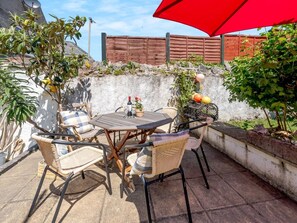 An outdoor patio with a round table, wicker chairs, and a red umbrella. - 3 Bed in Tenby (oc-fb189) (Tenby)