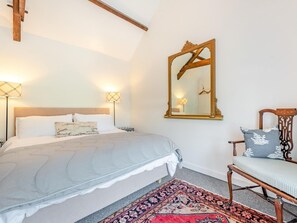 A bedroom with a bed, a chair, a large mirror, and a patterned rug. - 3 Bed in Tenby (oc-fb189) (Tenby)