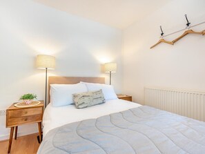 A neatly arranged bedroom with a bed, bedside tables, lamps, a radiator, and a wall-mounted hanger. - 3 Bed in Tenby (oc-fb189) (Tenby)