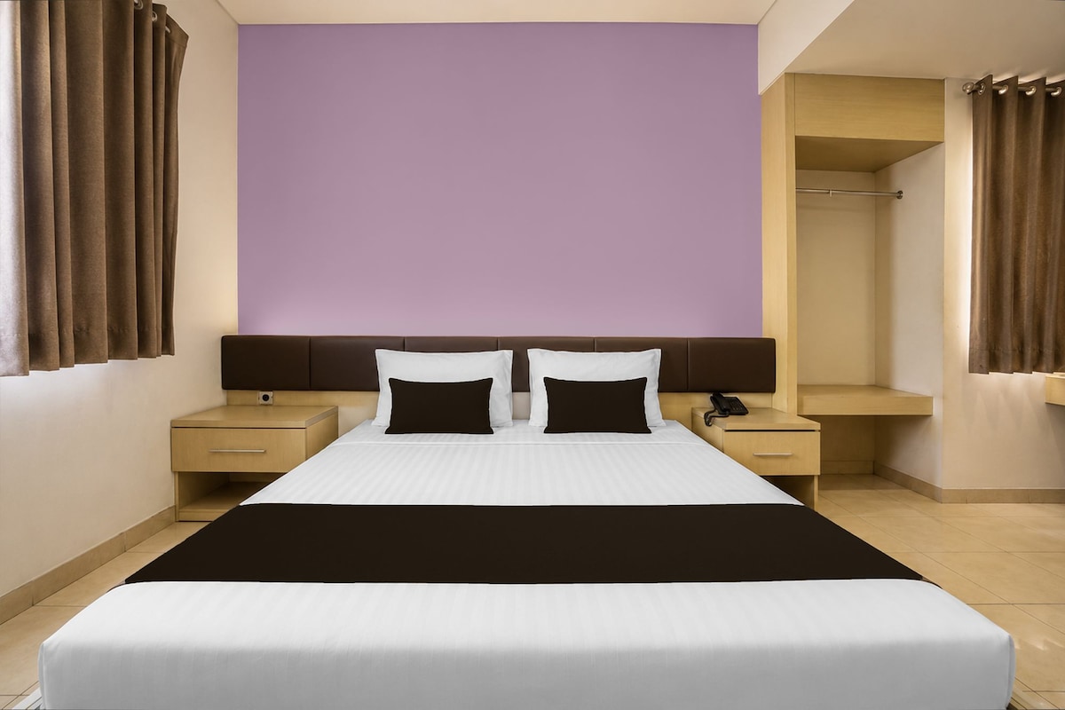 A hotel room with a large bed, two bedside tables, a wardrobe, and a bathroom.