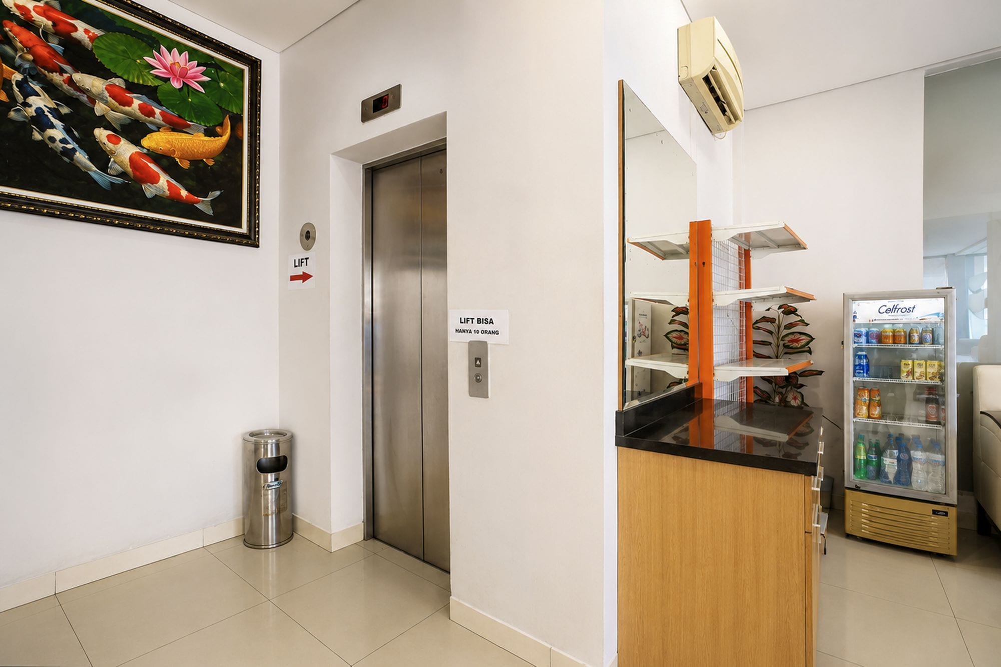 Un vestíbulo de hotel con ascensor, un bote de basura, una máquina expendedora y un refrigerador.