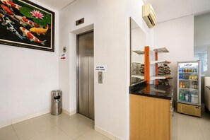 Um saguão de hotel com elevador, lixeira, máquina de vendas automática e refrigerador.