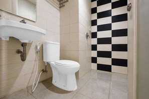 A bathroom with a toilet, sink, and checkered wall tiles. - Townhouse Oak Hotel Niaga Surabaya (Surabaya)