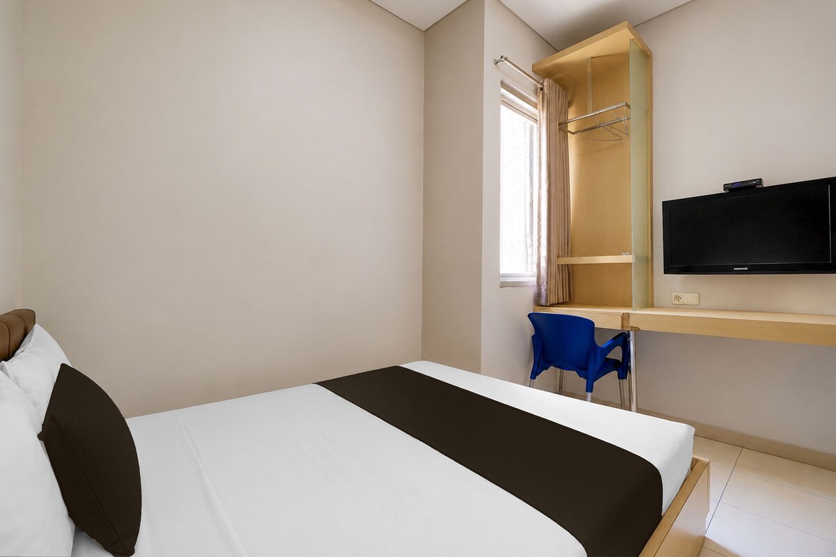 A hotel room with a bed, a desk with a chair, a television, and a window with curtains.