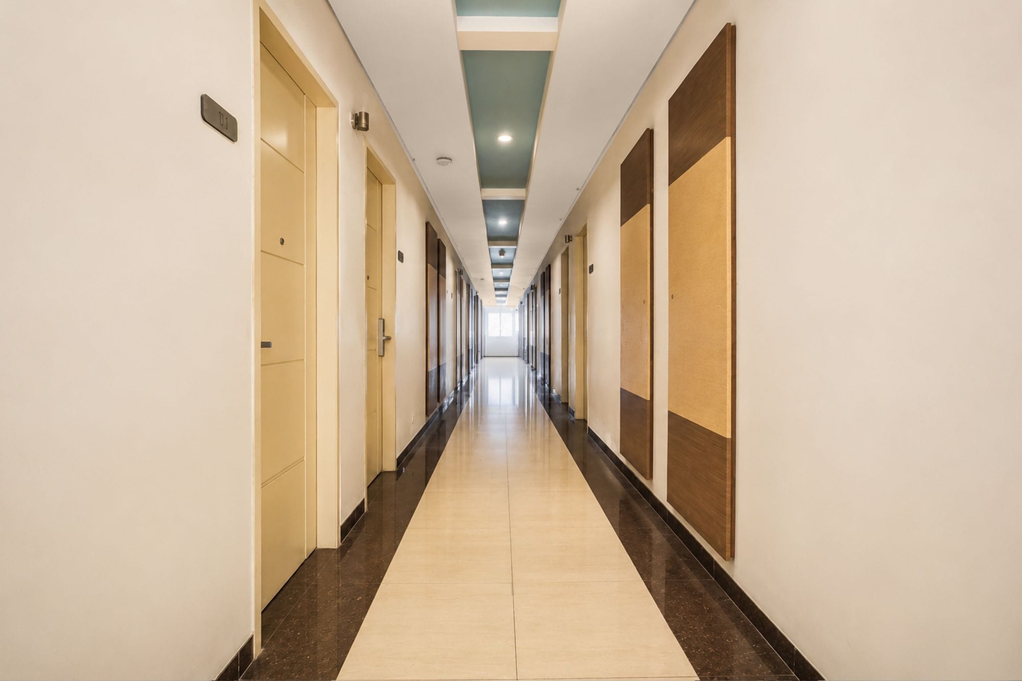 Un largo y estrecho pasillo de hotel con puertas a ambos lados, piso de baldosas e iluminación empotrada en el techo.