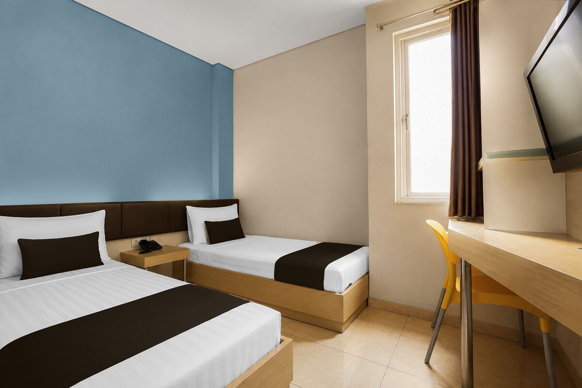 A hotel room with two beds, a desk, a chair, a television, and a window with curtains.