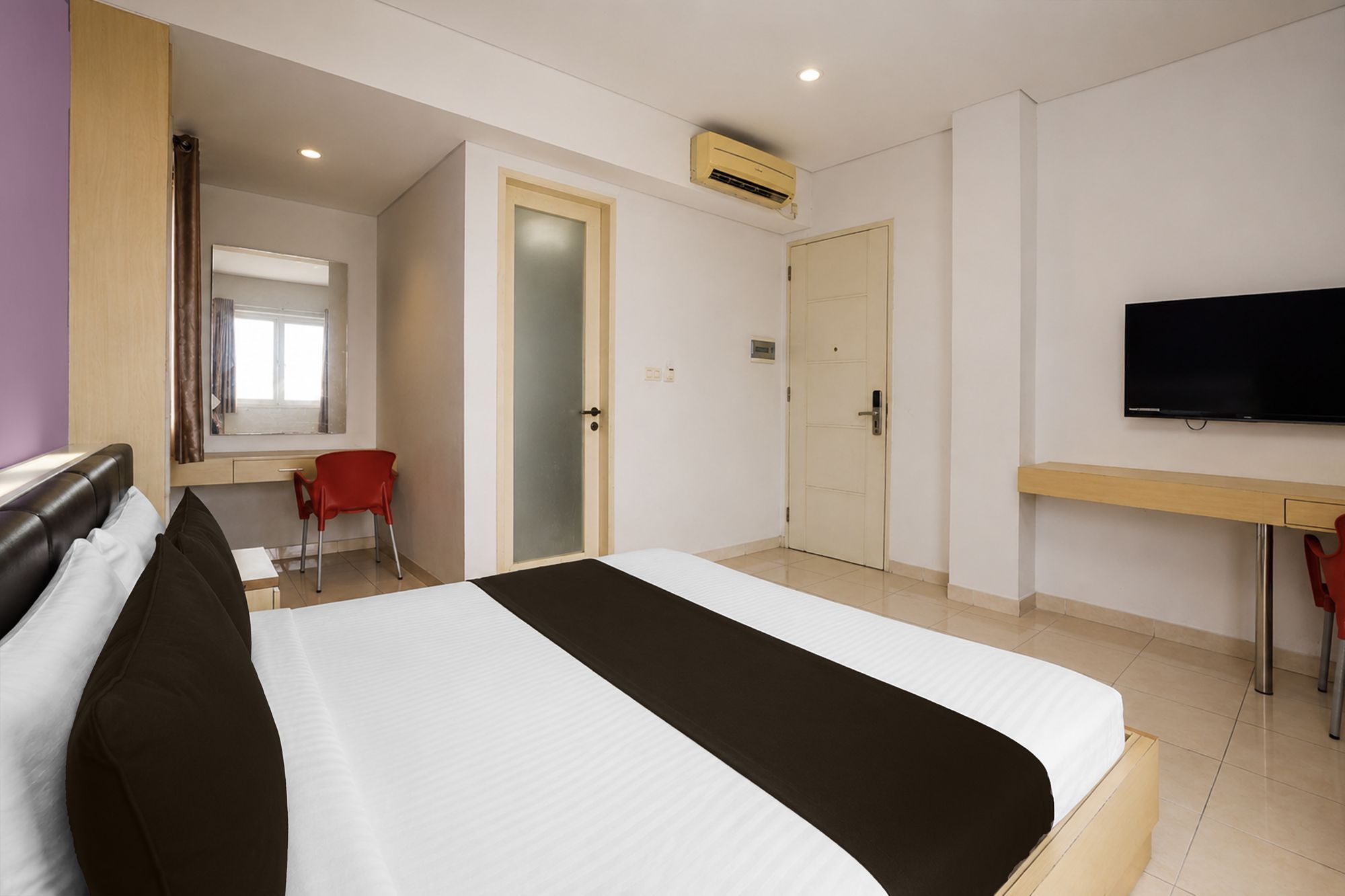 Habitación de hotel con cama, escritorio, silla, televisor y aire acondicionado.