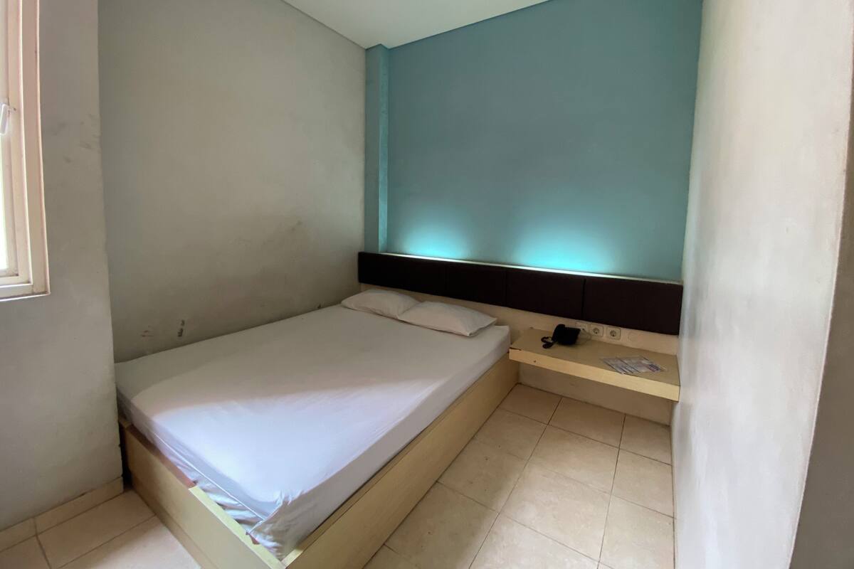Ein kleines Einzelzimmer mit einer schlichten weißen Wand, einer Akzentwand in Türkisgrün und einem Fenster auf der linken Seite.