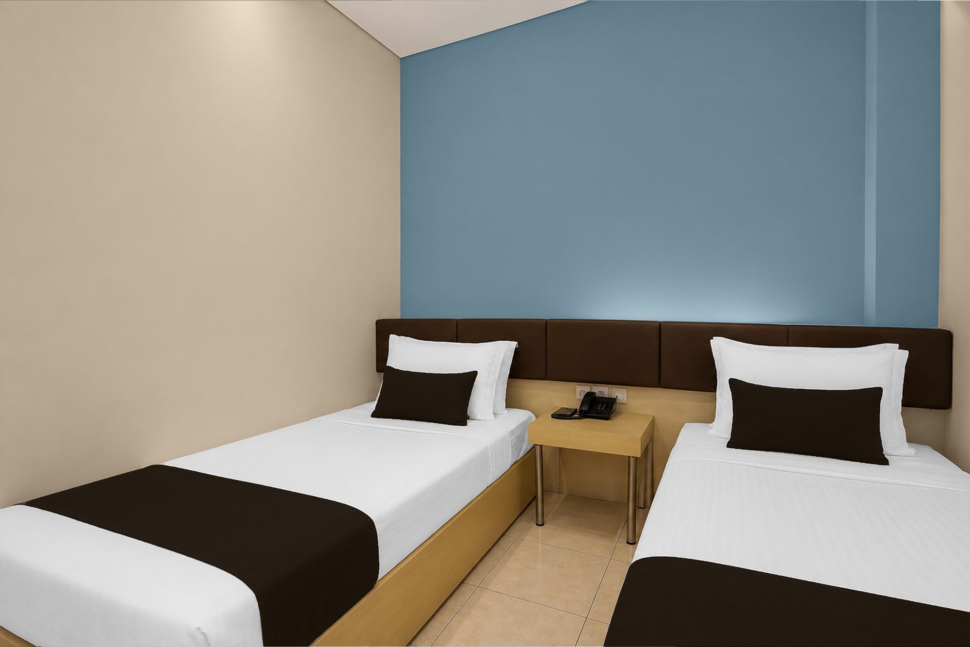 A hotel room with two single beds, a nightstand with a phone, and a blue accent wall.