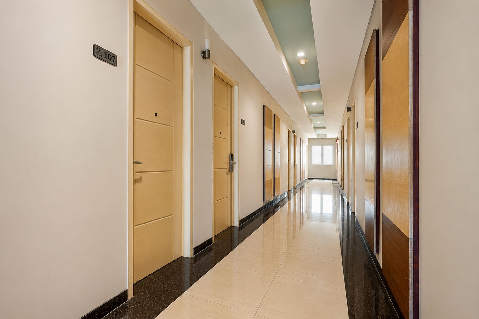 Un pasillo de hotel con puertas, suelo de baldosas e iluminación empotrada en el techo.