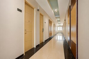 Corredor de hotel com portas, piso ladrilhado e teto com iluminação embutida.