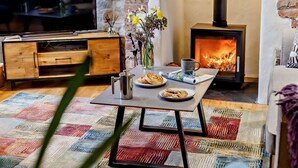 Ein gemütliches Wohnzimmer mit Fernseher, Tisch mit Tasse, Keksen und Blumenvase, Kamin und Steinwand.