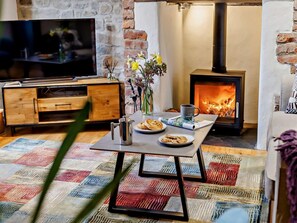 Ein gemütliches Wohnzimmer mit Fernseher, Tisch mit Tasse, Keksen und Blumenvase, Kamin und Steinwand.