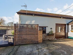 Una casa de una sola planta con fachada blanca, techo de tejas y puerta de madera, además de un ventanal pequeño.