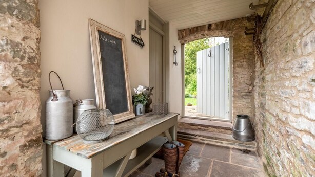 Een rustieke stenen muur, een houten bank met metalen bakken, een prikbord en een deur naar buiten.