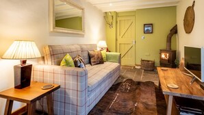 Een gezellige woonkamer met een geruit bankje, een houten tafel, een spiegel en een open haard.
