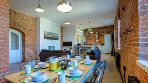 A dining area with a long table set for breakfast, a kitchen in the background, and brick walls. - 3 Bed in Freshwater (oc-78098) (Freshwater)