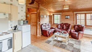 A log cabin interior with a kitchen, leather sofas, and a dining table.