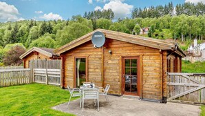 A wooden cabin with a satellite dish, a patio with chairs, and a wooden fence.