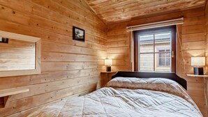 A wooden cabin room with a bed, two bedside tables, a window, and a picture on the wall.