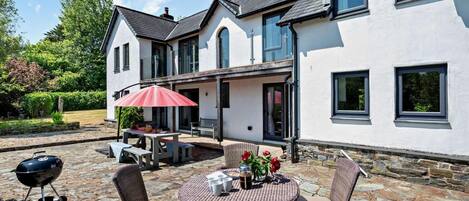 A house with a patio area featuring wicker furniture, a barbecue grill, and a red umbrella.