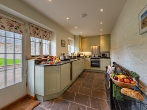 A spacious kitchen with a large island, a stone floor, and a view of the garden through the windows. - 2 Bed in Brecon (oc-42931) (Llanfrynach)