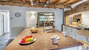 Une cuisine dotée d’un plan de travail en granit, de poutres en bois, d’une horloge et d’un mur en pierre rustique.