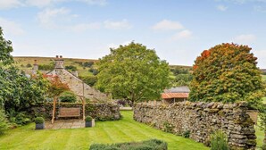 Une charmante maison en pierre avec un toit de chaume, entourée d’un jardin bien entretenu et de murs en pierre.